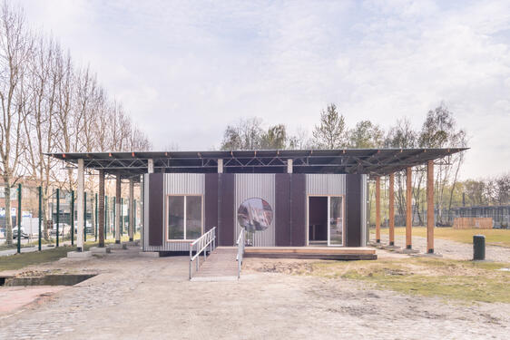 photo d'un bâtiment après livraison, on y distingue bien la toiture en tole, deux fenetres, une porte et une rangée de poteaux en bois